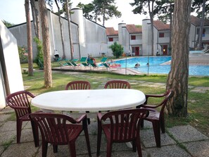 A pool area with lounge chairs and a table surrounded by trees. - Holiday Village by Interhome (Lignano Sabbiadoro)