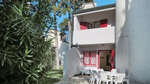 Un bâtiment à deux étages doté d’un balcon, de murs blancs et d’éléments décoratifs rouges. On y trouve une terrasse avec des chaises et une table en plastique blanc.
