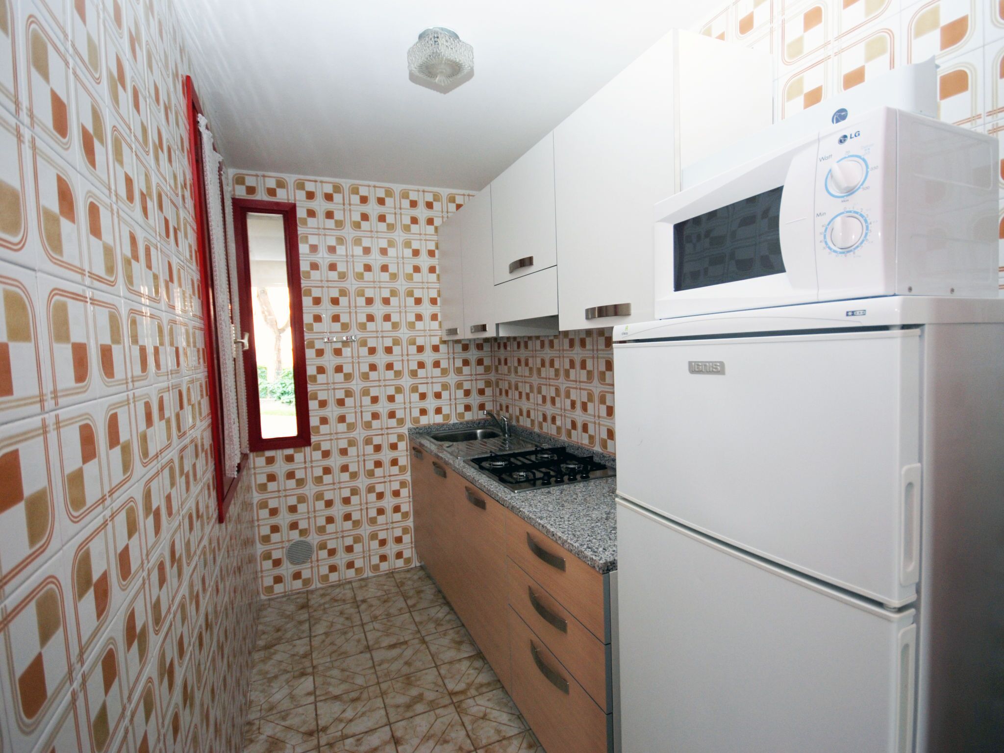 A compact kitchen with patterned tiles, a built-in microwave, and a refrigerator.