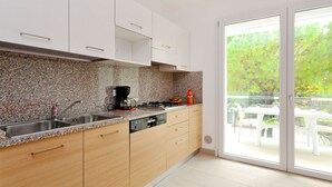 A modern kitchen with granite countertops, a coffee maker, and a sink. There is a sliding glass door leading to an outdoor area with a table and chairs. - Apartment Fiore by Interhome (Lignano Sabbiadoro)