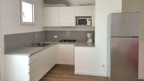 A compact kitchen with white cabinets, a granite countertop, a stainless steel refrigerator, a microwave, and a gas stove.