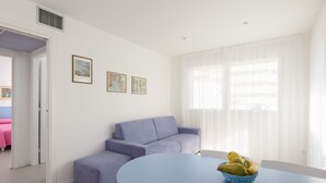 A modern living room with a blue sofa, a round table with a fruit bowl, and two framed pictures on the wall. - Residenza Edda by Interhome (Lignano Sabbiadoro)