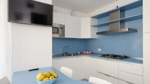 A modern kitchen with white cabinets, a blue countertop, a gas stove, a microwave, and a TV mounted on the wall. - Residenza Edda by Interhome (Lignano Sabbiadoro)