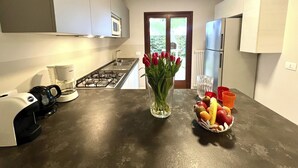 A modern kitchen with a gas stove, a coffee maker, a bowl of fruit, and a vase of red tulips.