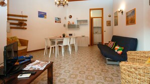 A compact living space with a dining area, a sofa, a TV, and a kitchen visible through an open door. - Villa Ralph by Interhome (Lignano Riviera)