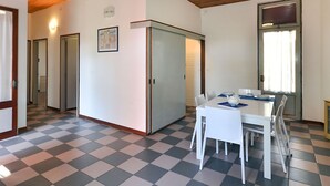 Une pièce avec un sol à carreaux, une table à manger avec des chaises, un réfrigérateur et une fenêtre avec des rideaux.