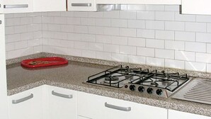Une cuisine avec des meubles blancs, une cuisinière à gaz et un plateau rouge posé sur le plan de travail.