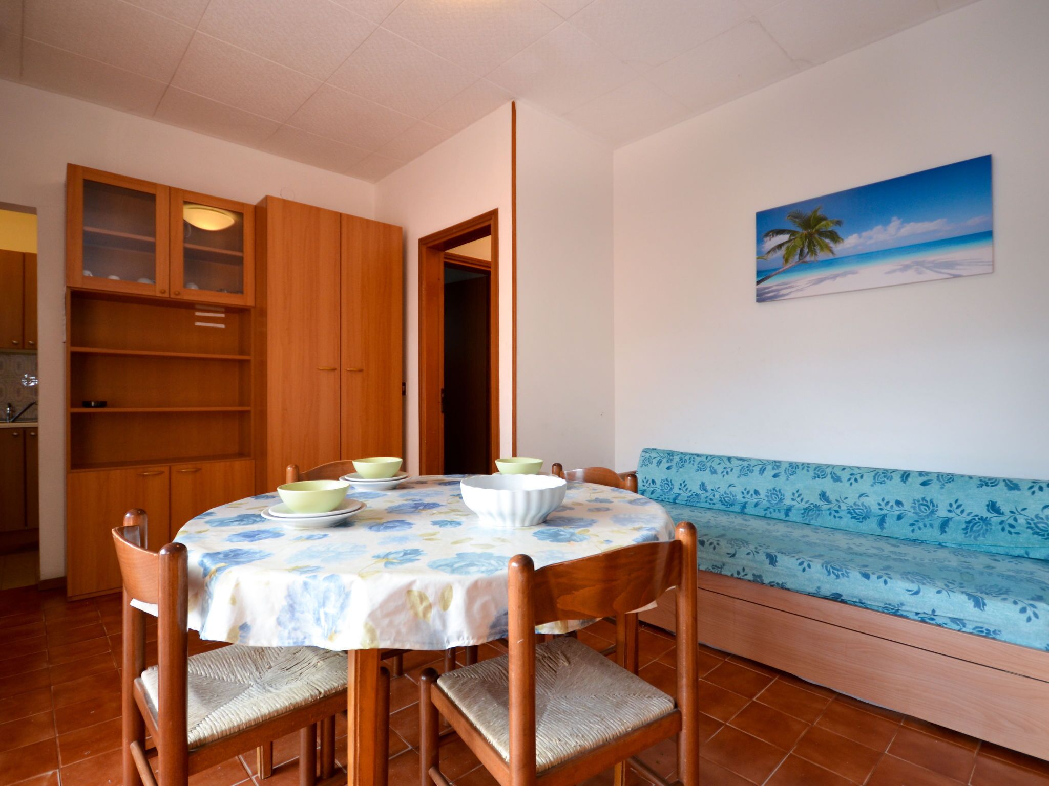 Un área de comedor con una mesa redonda, sillas y un sofá. Hay un cuadro de una playa en la pared.