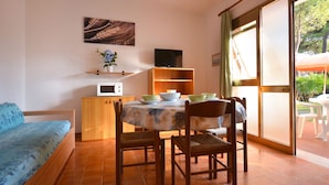 Un salon confortable avec un canapé, une table à manger et des chaises, un four à micro-ondes, un téléviseur et une fenêtre donnant sur un paysage verdoyant.