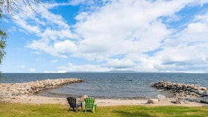 En strand med två stolar som är placerade mot vattnet, en stenig kustlinje och en klar himmel.