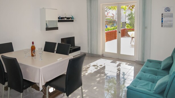 Uma zona de refeições moderna com uma mesa posta para quatro pessoas, um sofá e uma porta de correr de vidro que dá para um alpendre.