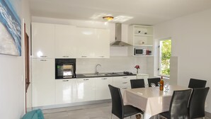 Uma cozinha moderna com armários brancos, forno embutido e um espaço de refeições com mesa e cadeiras.