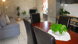 Una sala de estar con sofá, mesa de comedor, sillas, televisor y una zona de cocina con refrigerador y estufa.