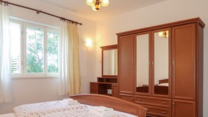Une chambre à coucher avec un lit en bois, une grande armoire, un miroir et une fenêtre avec des rideaux.
