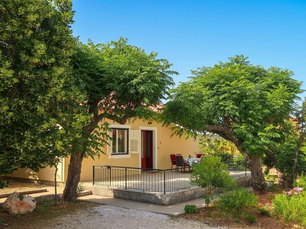 A building with a yellow facade, a red door, and a covered outdoor seating area with tables and chairs. - Vacation home Andela by Interhome (Rab/Rab)