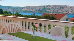 A balcony with a table, chairs, and a vase with a flower. It overlooks a scenic view of a body of water and hills. - Apartment Matius by Interhome (Rab/Rab)