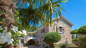 A stone house with a covered patio, a small garden, and a palm tree. - Apartment Mia by Interhome (Krk/Malinska)