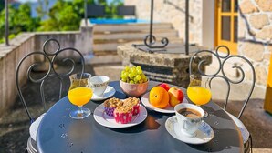 A table set with breakfast items including fruits, muffins, coffee, and juice, outdoors with a stone building and pool in the background. - Apartment Mia by Interhome (Krk/Malinska)