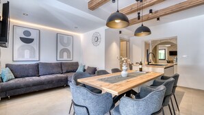 Un salon moderne avec une table à manger en bois, des chaises à revêtement gris, un canapé gris et une cuisine en arrière-plan.