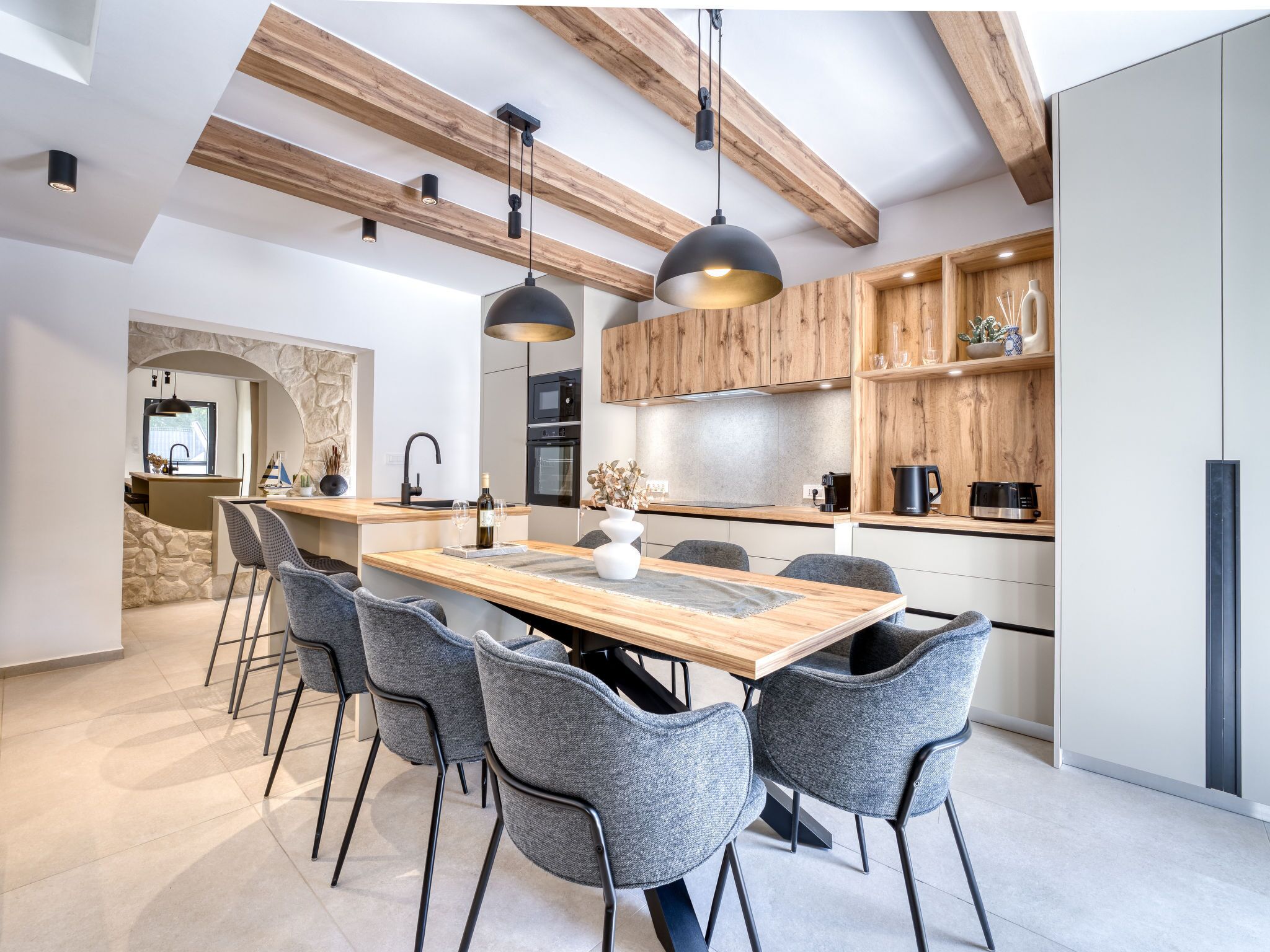 A modern kitchen with a wooden island, grey chairs, pendant lights, and built-in wooden cabinets.