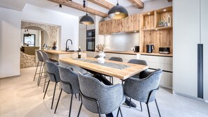 Une cuisine moderne avec un îlot central en bois, des chaises grises, des luminaires suspendus et des meubles de rangement en bois intégrés.