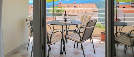 En balkon med et bord og stole, to grønne parasoller og udsigt til bygninger og bakker.