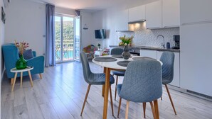 Eine moderne Küche mit weißen Schränken, ein Essbereich mit rundem Tisch und grauen Stühlen sowie ein Balkon mit Seeblick.