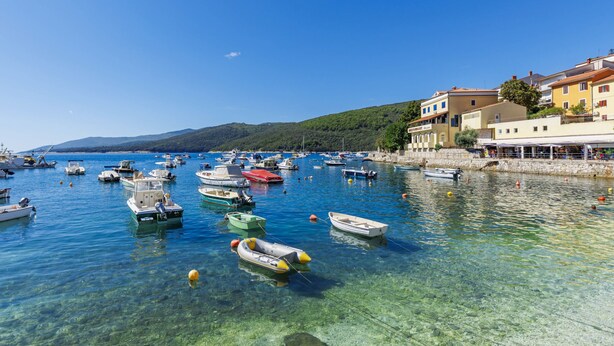 A marina with various boats, clear water, and buildings with a restaurant named "RESTAURANT Azzurro" on the right.