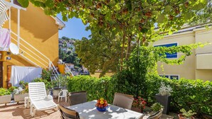 An outdoor patio with a table and chairs, surrounded by potted plants and a tree with fruit.