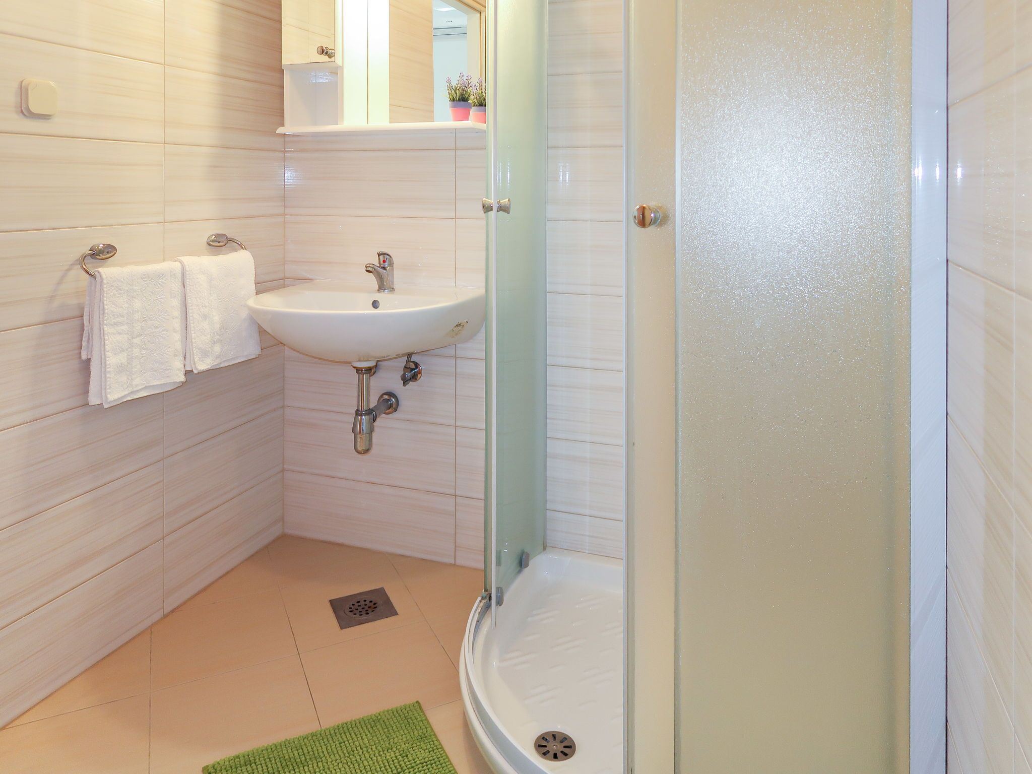 A bathroom with a white sink, a glass shower enclosure, and a green bath mat.