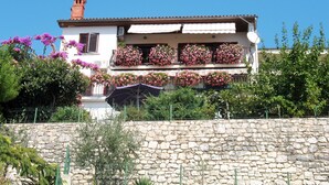 A two-story building with balconies adorned with pink flowers, a stone wall in the foreground, and a clear blue sky. - Apartment Neda by Interhome (Rabac)