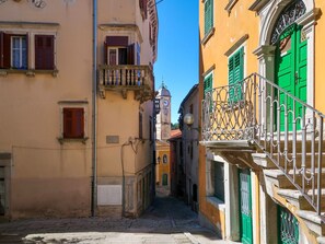 A narrow street with buildings on either side, featuring balconies and a clock tower in the background. - Vacation home Carla by Interhome (Labin)