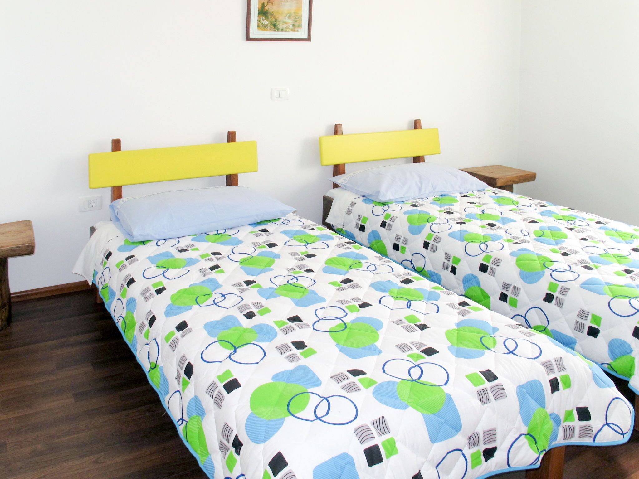 A double room with two single beds, each with a yellow headboard, white bedding with green and blue patterns, and wooden nightstands.
