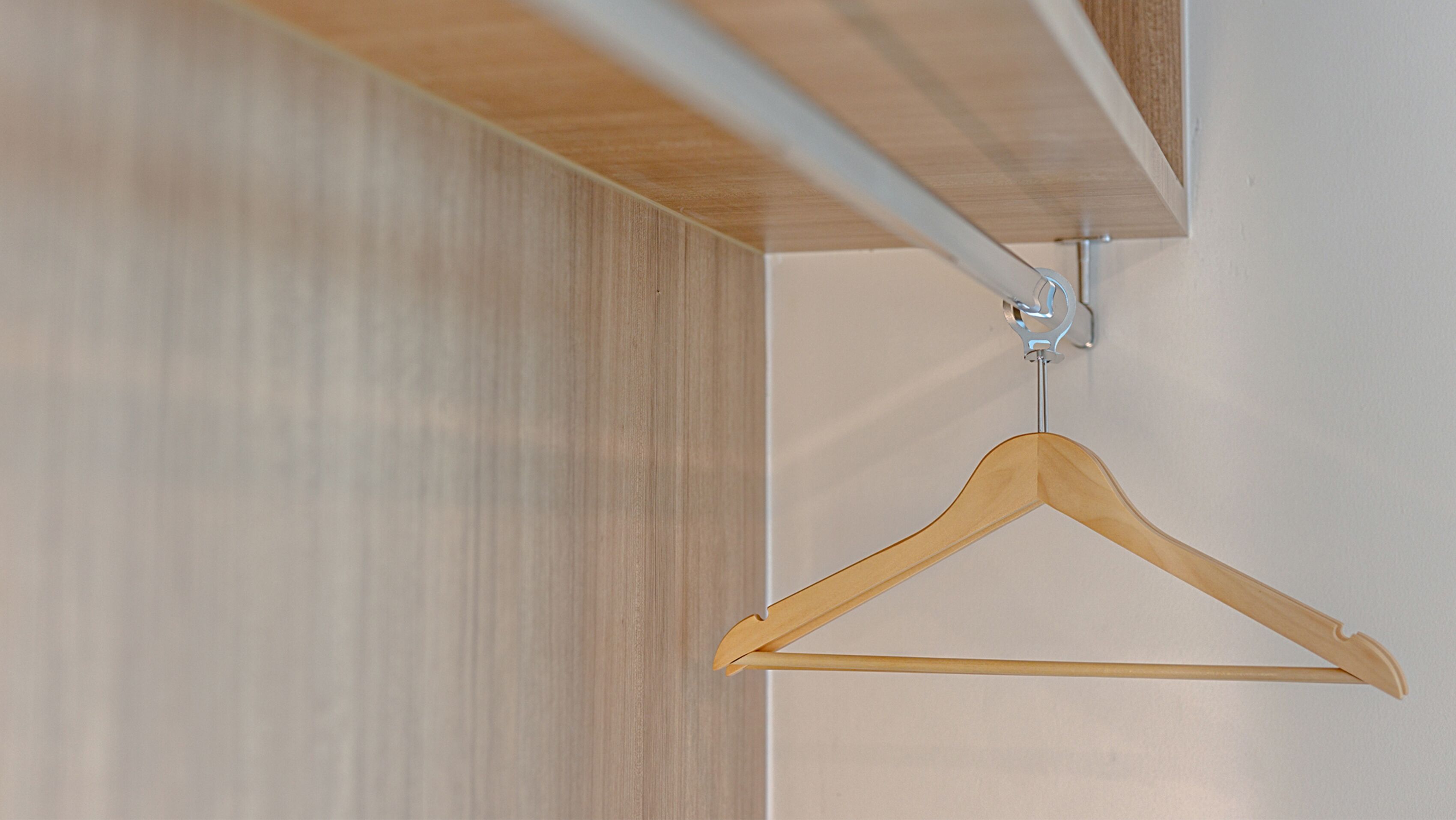Una percha de madera en un gancho metálico fijado a una pared blanca.