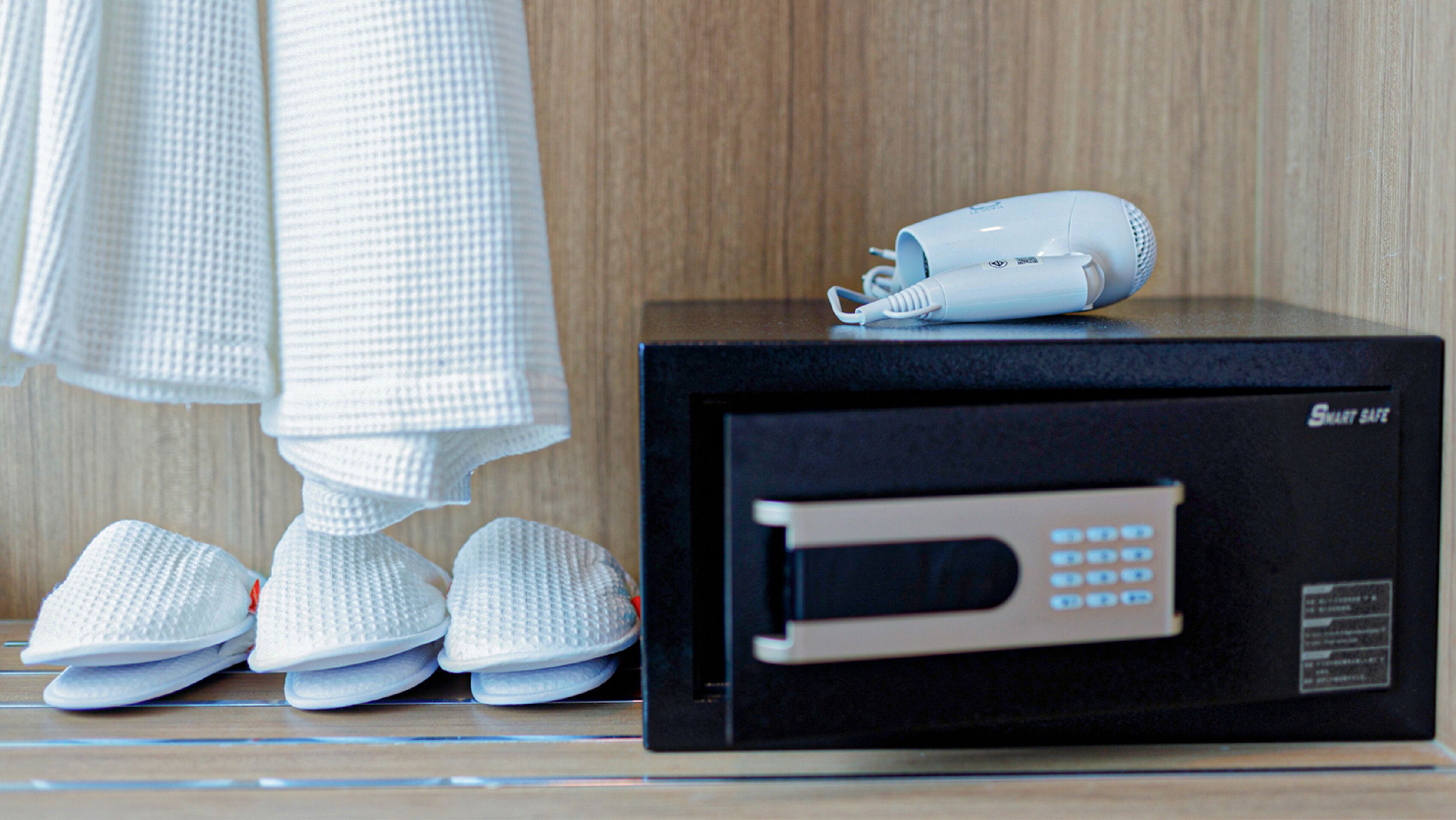 A black appliance with a digital display and a control panel, a white hairdryer, and a pair of white slippers on a wooden surface.