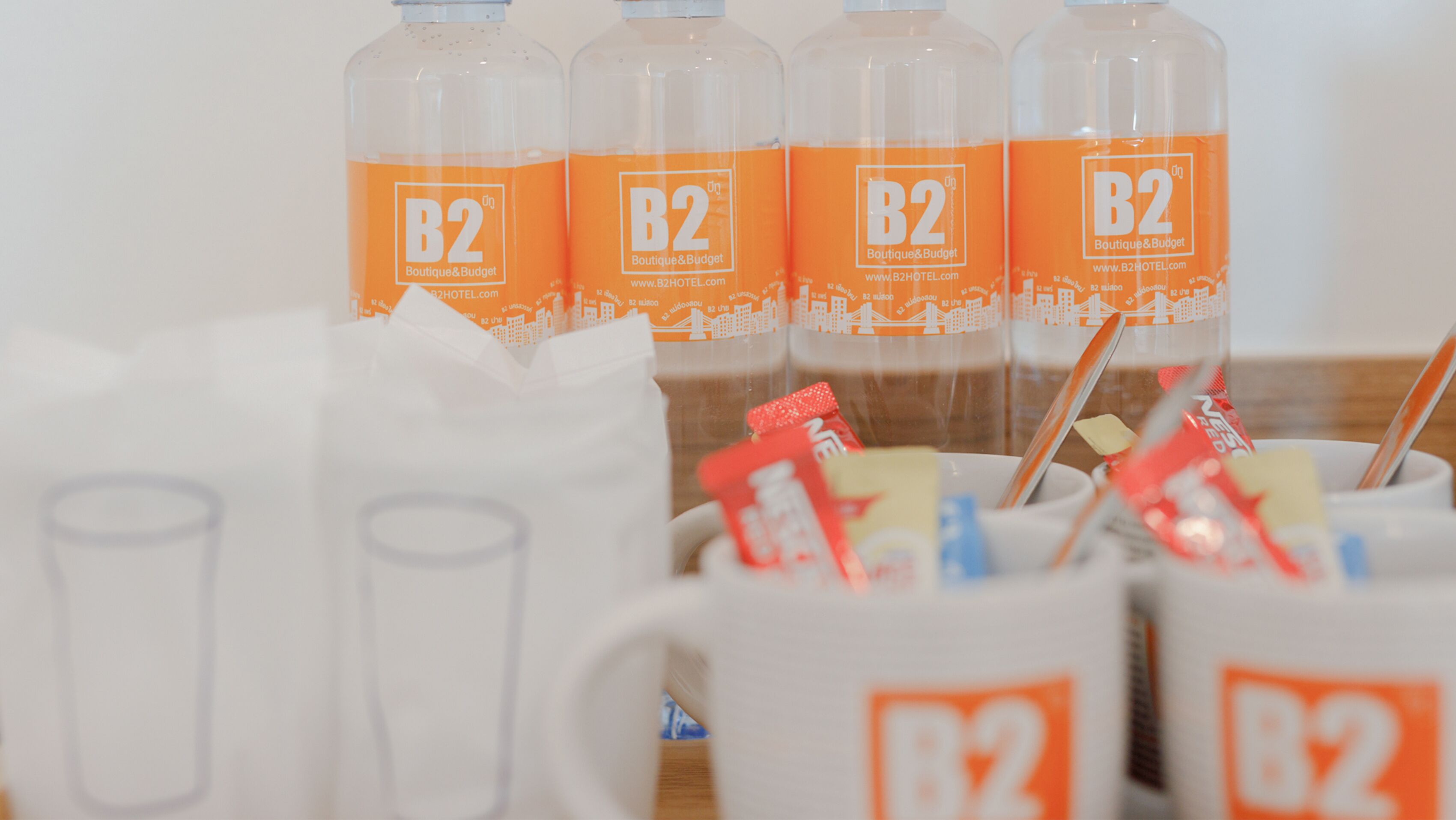 Una mesa con varias tazas blancas y botellas con la etiqueta B2 Boutique & Budget.