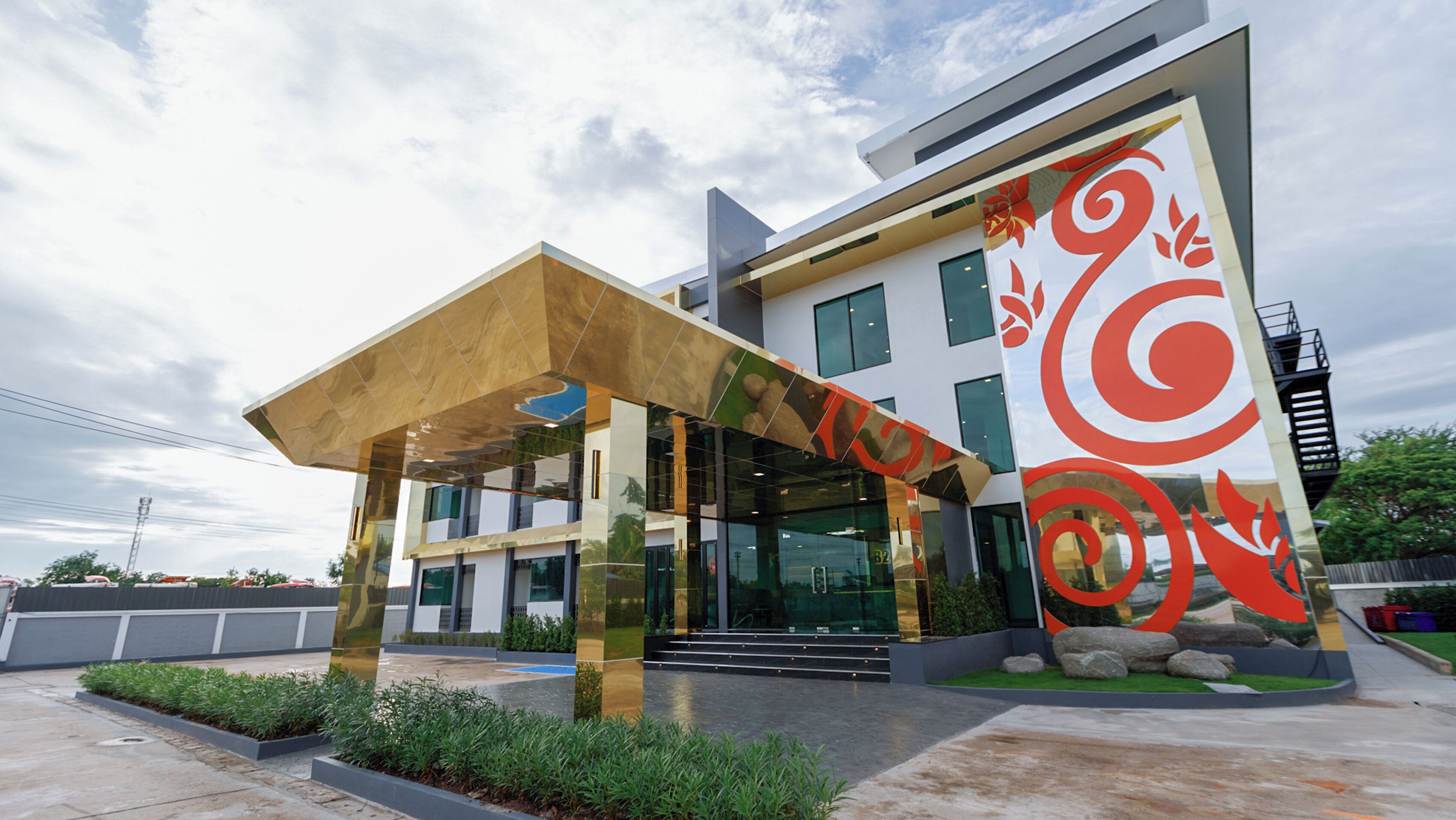 A modern building with a glass facade, a covered entrance, and a distinctive red and white design on the side.