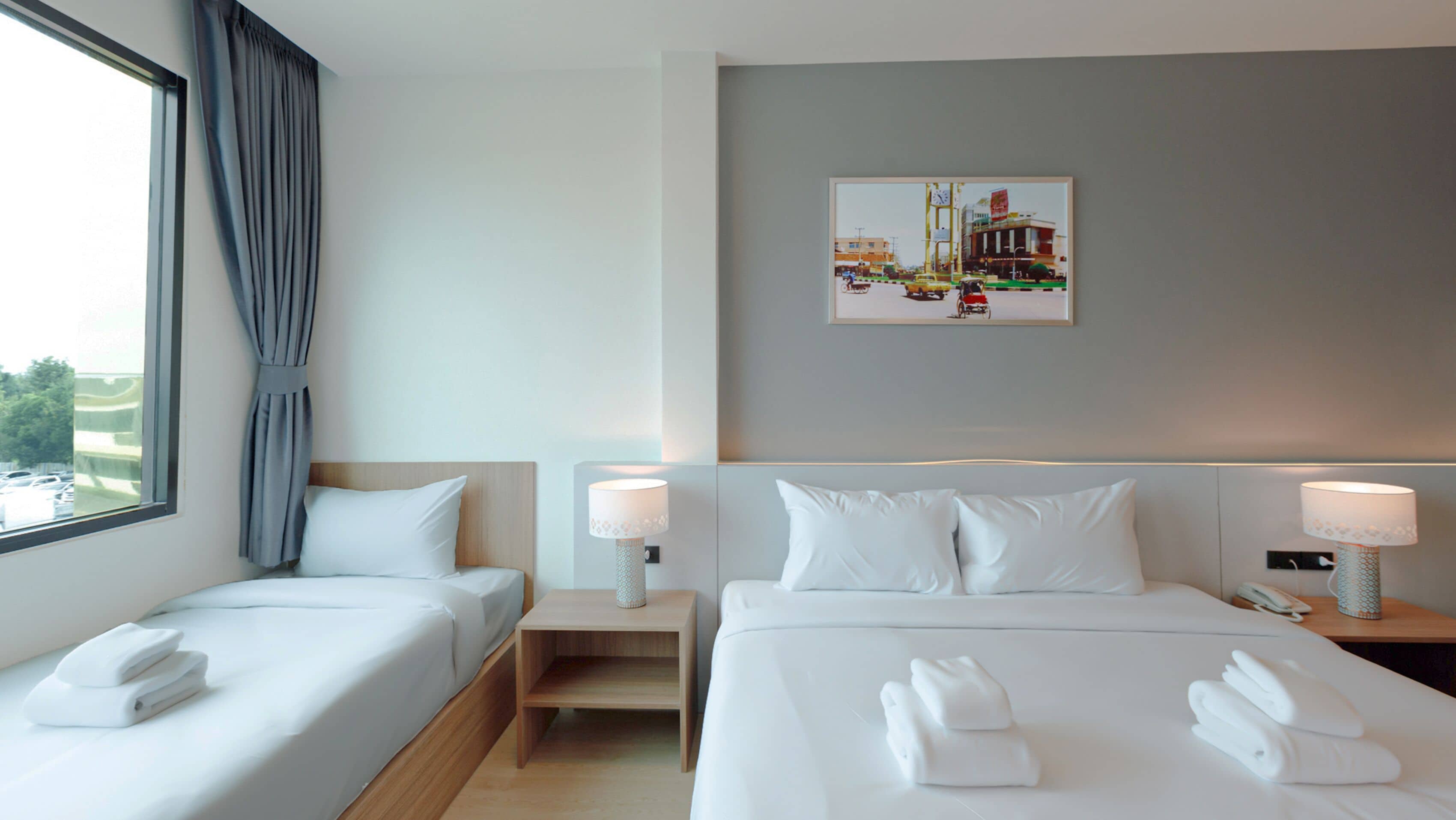 A hotel room with two beds, a painting on the wall, and a window with curtains.