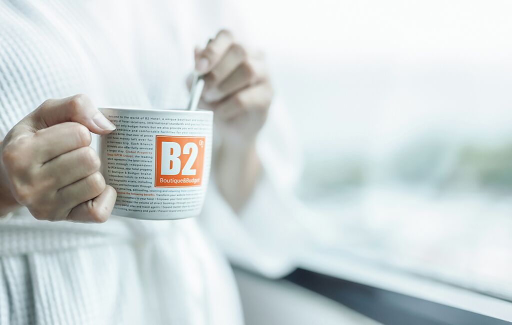 A person holding a mug with the text "B2 Boutique&Budget" on it.