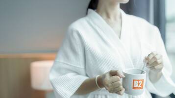 A person in a white robe holding a mug with a spoon, in a room with a window and a lamp.