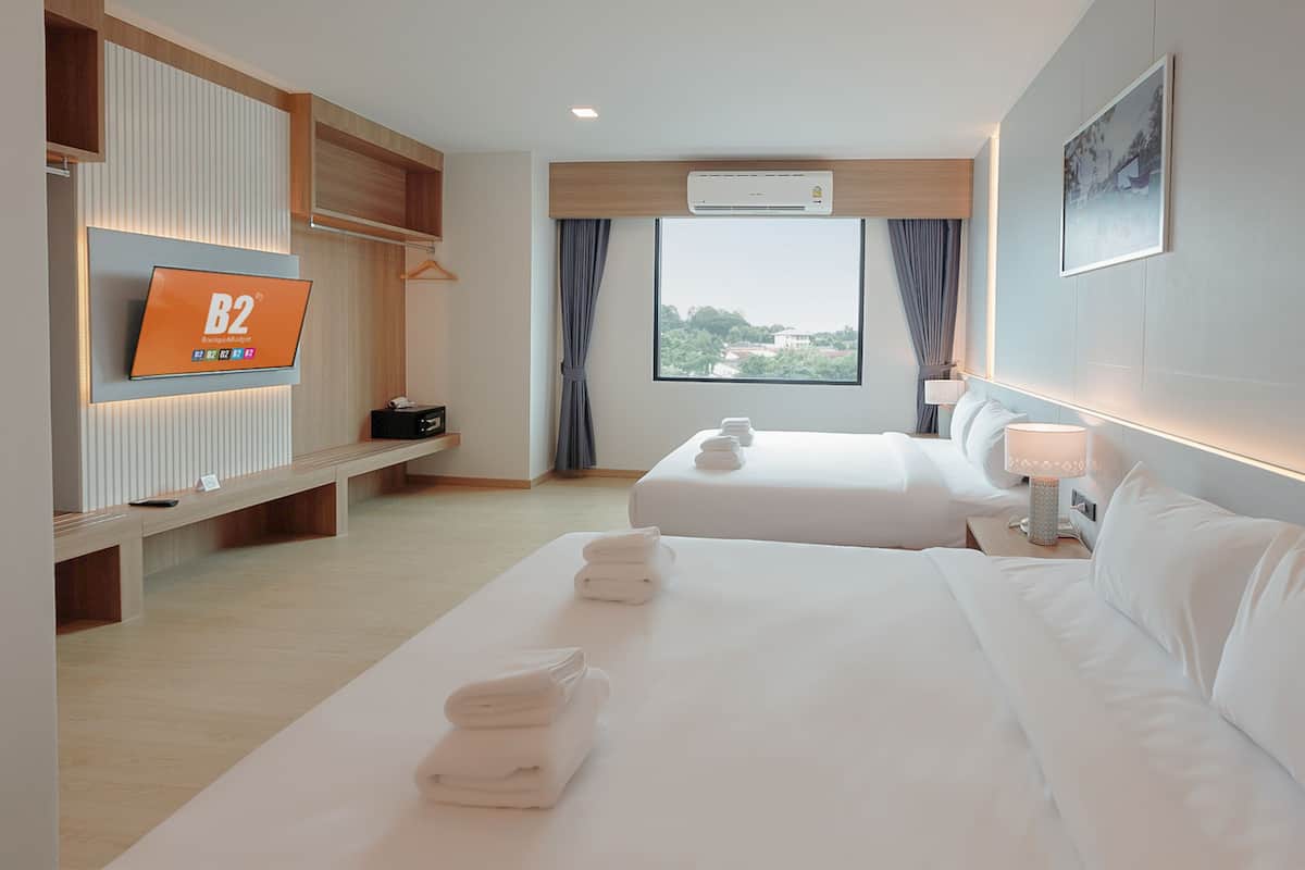 Una habitación de hotel con dos camas, televisión, ventana con vistas y mesita de noche con lámpara.