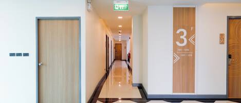 Pasillo de hotel con piso a cuadros, una puerta de madera a la izquierda y una pared con números de habitación y señal de salida.