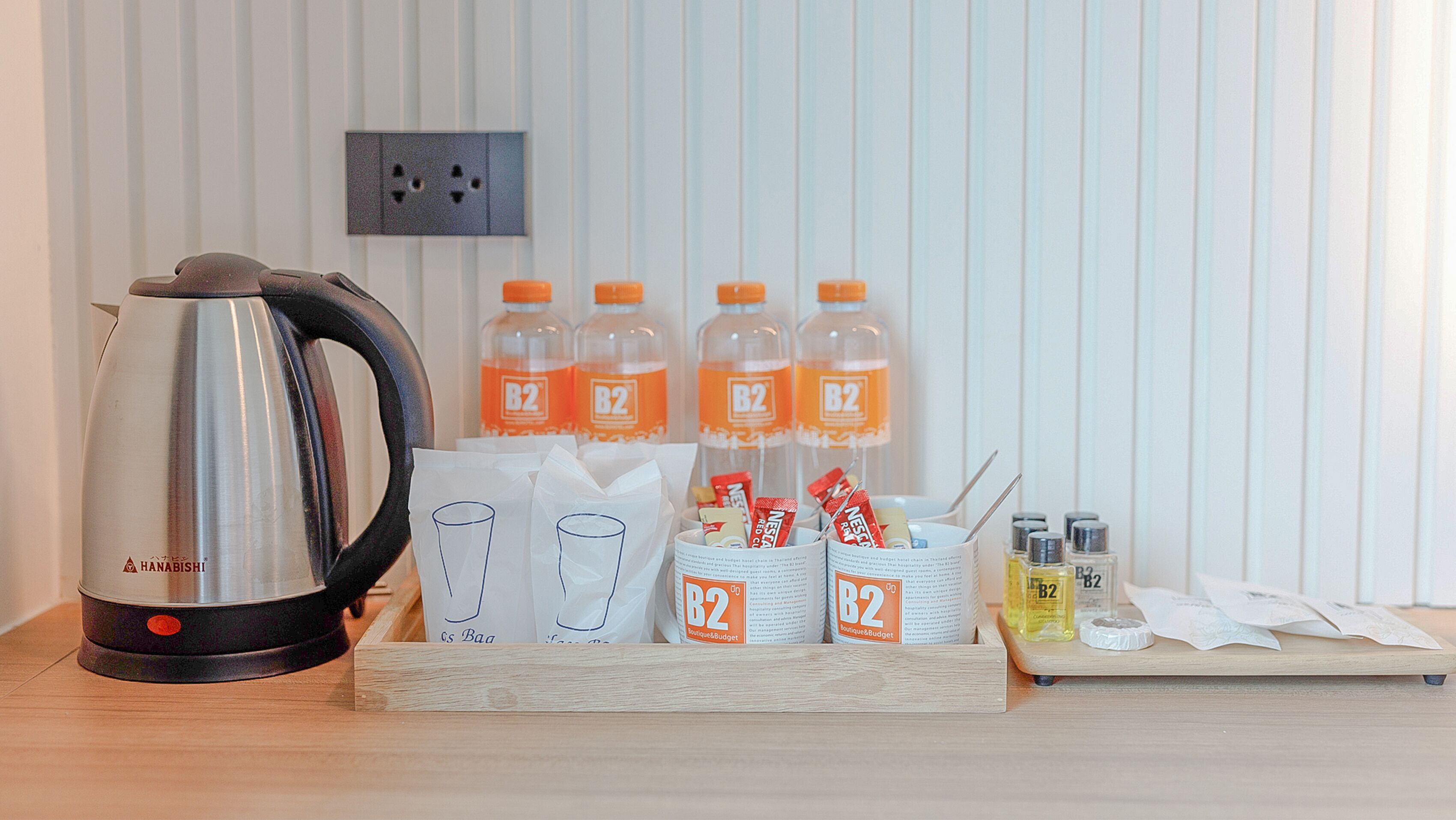 A kitchenette with a kettle, water bottles, coffee packets, and condiments.