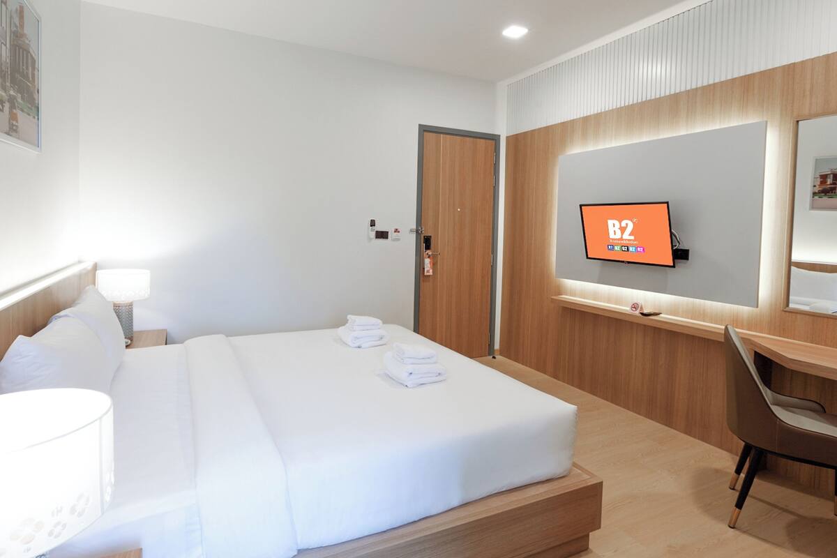 Habitación de hotel con cama, escritorio, silla, televisor y puerta.