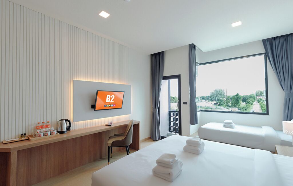 A hotel room with a TV, a desk with a chair, two beds, and a window with curtains.