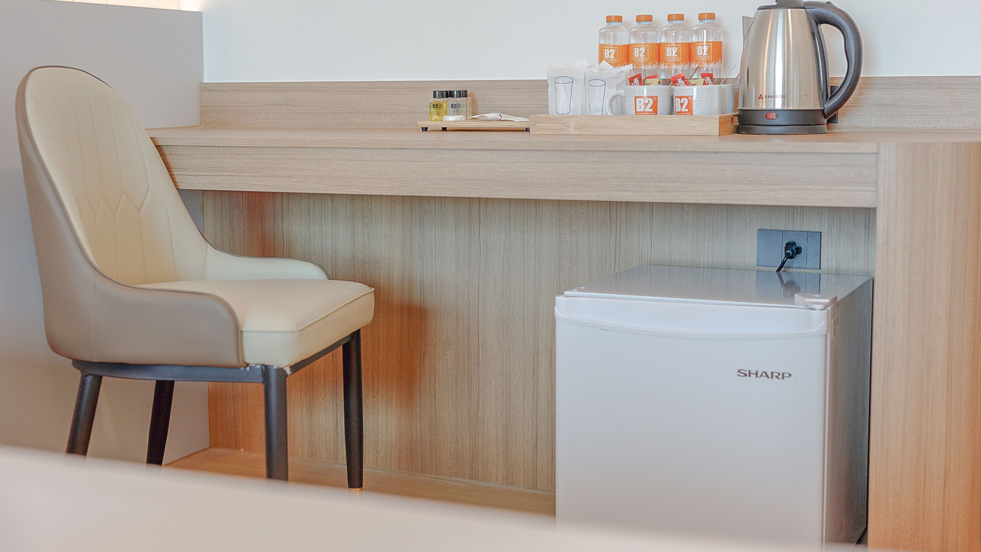 Una kitchenette compacta con una silla, un refrigerador pequeño, una cafetera y algunos condimentos sobre la encimera.