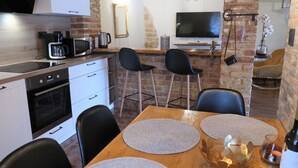 Eine moderne Küche mit Mikrowelle, Kaffeemaschine und Backofen. Es gibt einen Essbereich mit einem Holztisch und Stühlen sowie einen an der Wand montierten Fernseher.
