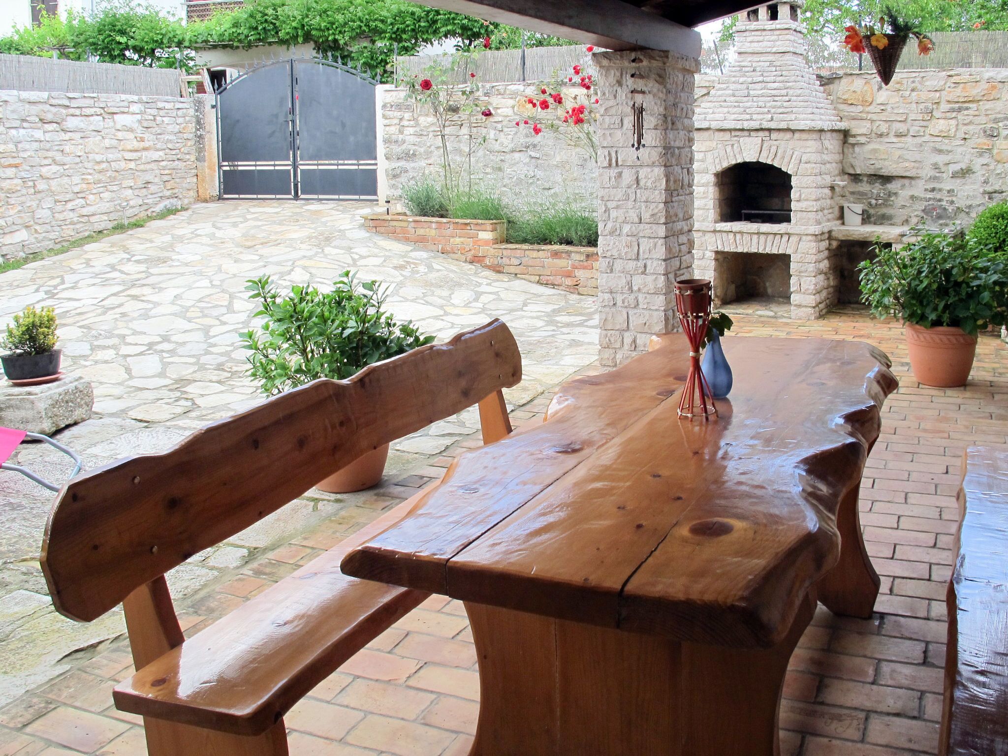 Um banco e uma mesa de madeira em um pátio de pedra, com uma parede de pedra e um forno de tijolos.