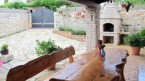 Eine Holzbänke und ein Holztisch in einem von Stein gepflasterten Patio mit einer Steinmauer und einem Backofen aus Ziegeln.