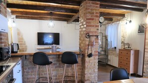 Eine Küche mit Fernseher, zwei Barhocker, einem Holztisch und einer Ziegelstütze.